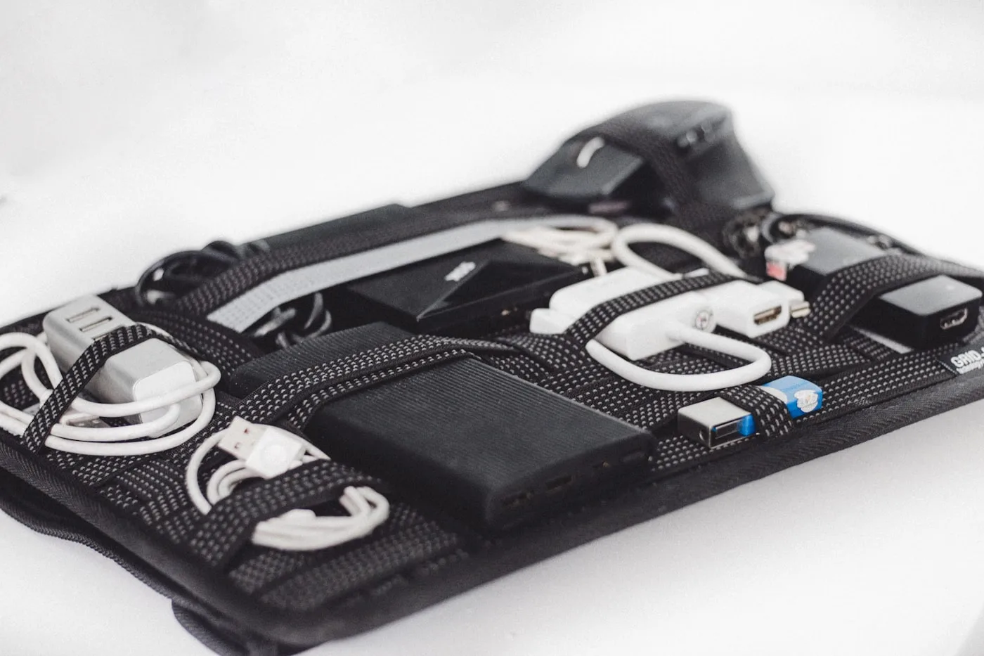 白い背景に置かれたガジェット整理ポーチ。中央に複数のUSBポートを備えた黒いモバイルバッテリーが固定され、周囲に充電ケーブルやUSBハブが並んでいる